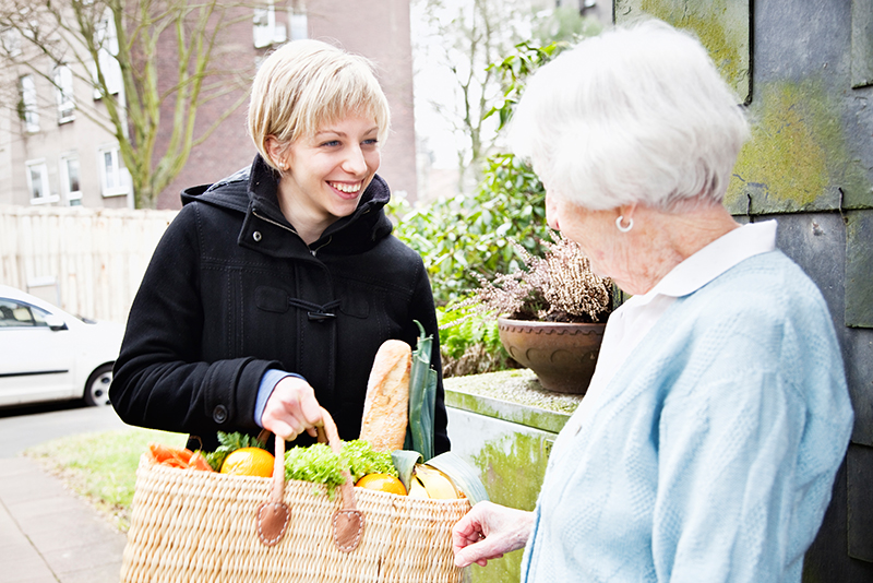 Eine 89-jährige Seniorin betrachtet die Einkäufe, die ihr von einer jungen Freiwilligen/Hauspflegerin nach Hause gebracht wurden.