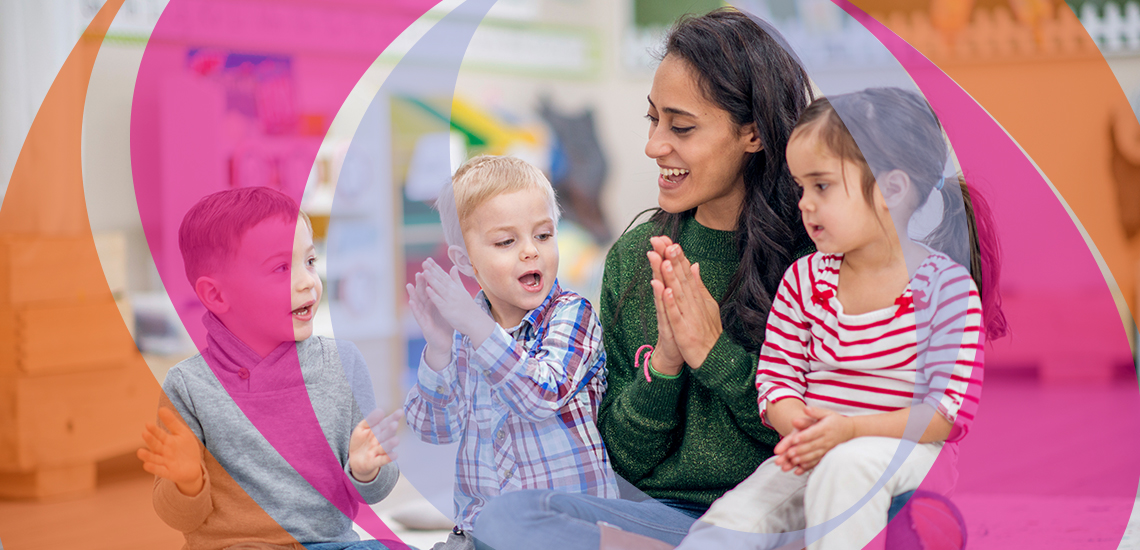 Eine Gruppe Vorschulkinder ist mit einer Ehrenamlichen drinnen. Sie sitzen auf dem Boden und klatschen zur Musik.